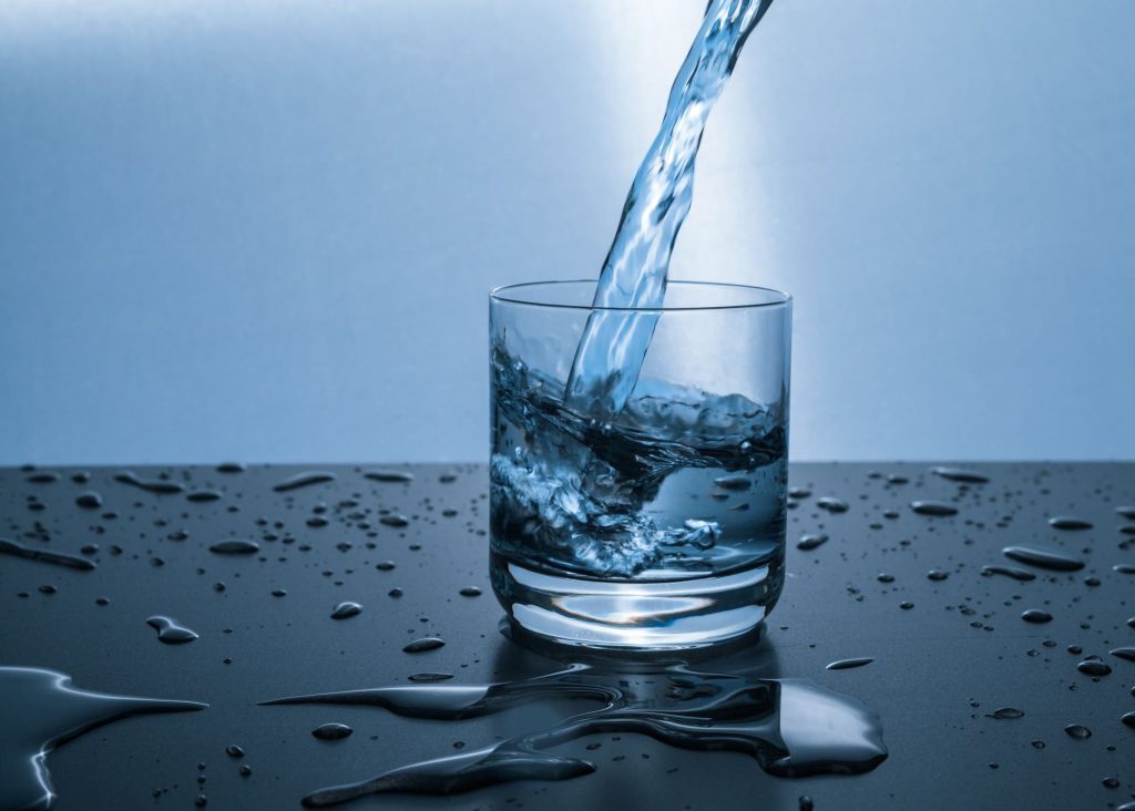 Puolitäysi vesilasi, johon valuu lisää vettä.